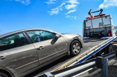 A car with an obscured license plate is towed by the MTA on a sunny day.